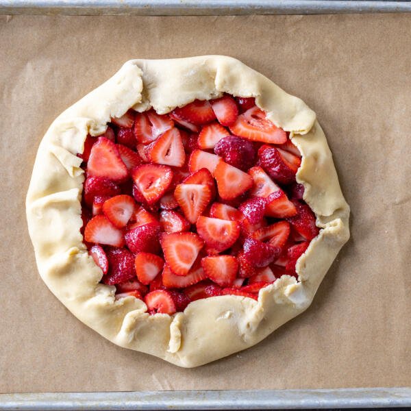 Shaped galette with strawberries on a baking sheet.