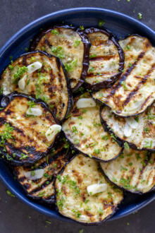 Grilled eggplant on a plate with garlic and herbs.