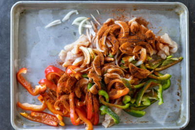 Chicken, veggies and seasoning in a sheetpan.