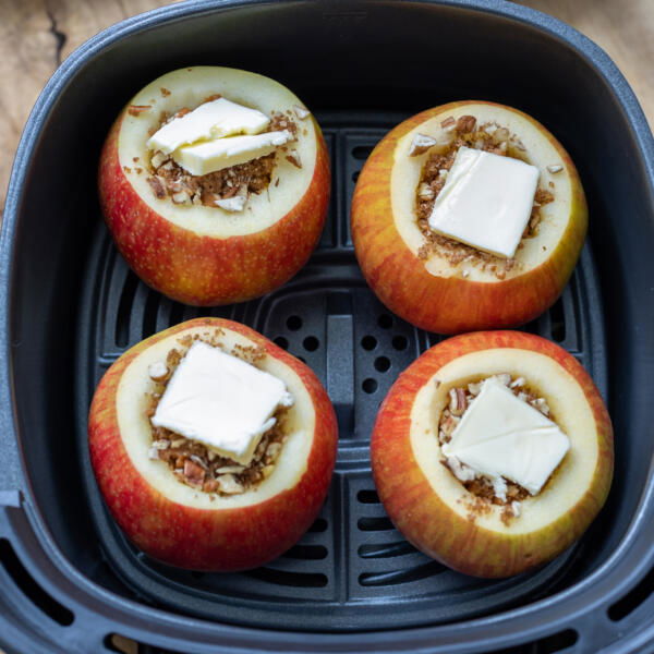 Apples with filling and butter on top in an air fryer basket.