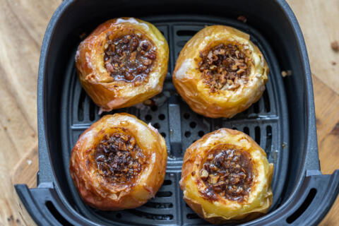 Apples in air fryer basket and nuts inside apples.