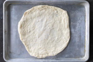Rolled out pizza dough on a baking sheet.