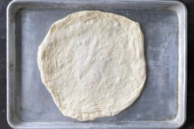 Rolled out pizza dough on a baking sheet.