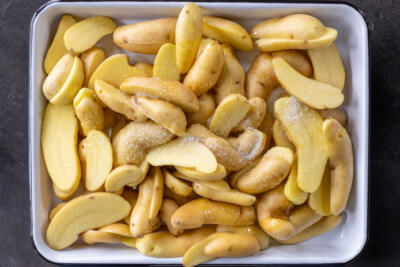 Sliced up potatoes with seasoning on a tray.