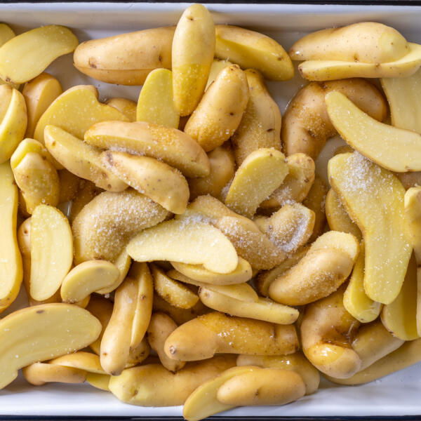 Sliced up potatoes with seasoning on a tray.