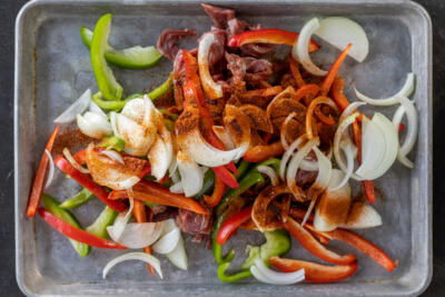 Steak, veggies and seasoning on a pan.