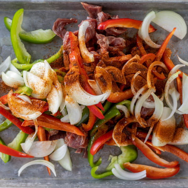 Steak, veggies and seasoning on a pan.