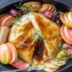 Baked Brie In Puff Pastry on a pan with fruits and crackers.