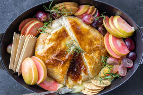 Baked Brie In Puff Pastry on a pan with fruits and crackers.