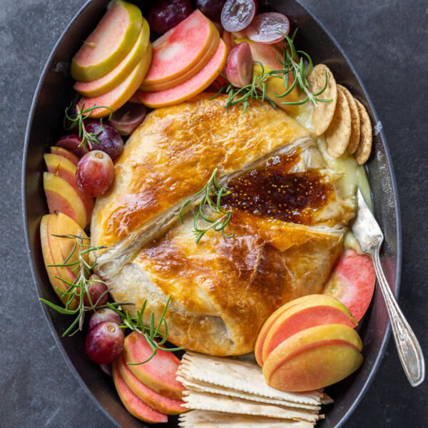 Baked Brie In Puff Pastry on a serving tray with other crackers and fruits.