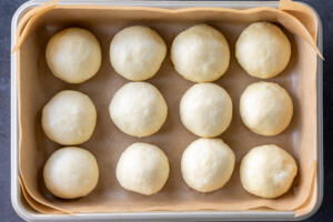 Brioche dinner rolls on a baking pan.