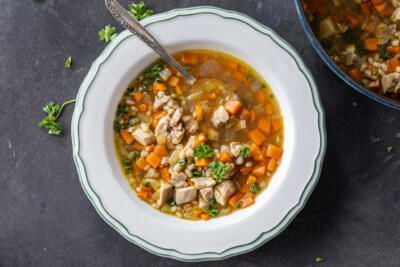 A bowl of Chicken Barley Soup with spoon and herbs around.