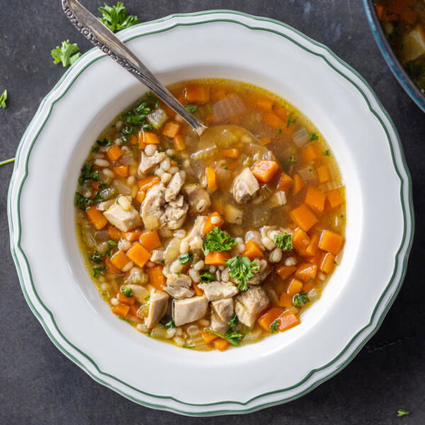 A bowl of Chicken Barley Soup with spoon and herbs around.