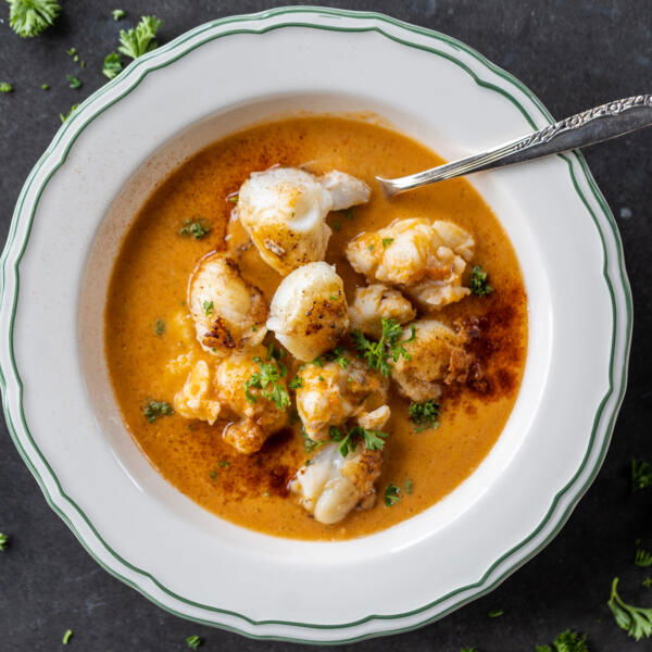 Creamy Lobster Bisque in a bowl with more lobster on top and herbs.