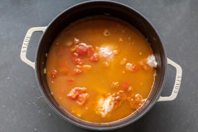 chicken added to veggies and broth in a pot.