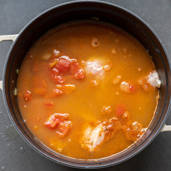 chicken added to veggies and broth in a pot.
