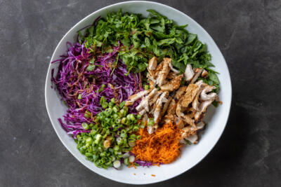 A serving bowl with Asian Chicken Salad and dressing on top.