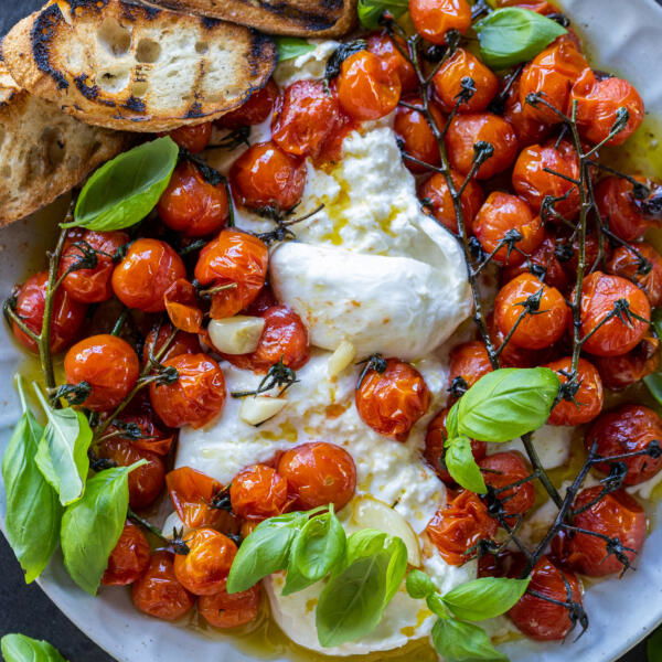 Braised Tomatoes with Burrata on a on a plate with basil and bread.