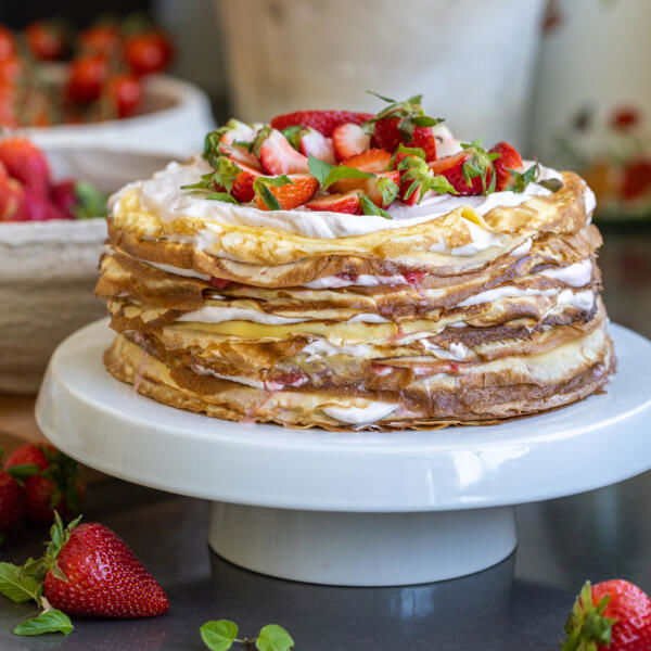 Strawberry Crepe Cake on a cake stand with berries around.
