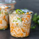 Jar with Curtido and herbs around.