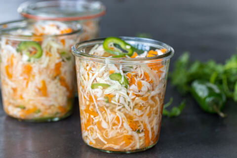 Jar with Curtido and herbs around.