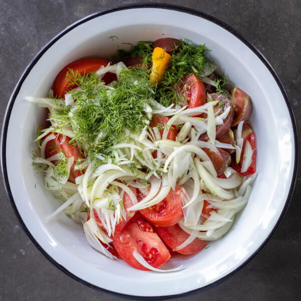 Tomatoes, onion, dill and seasoning in a bowl.