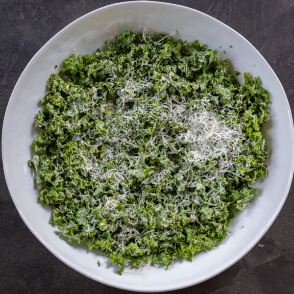 Kale, dressing and parmesan in a bowl.
