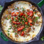 Queso Fundido in a skillet with herbs and tomato toppings.