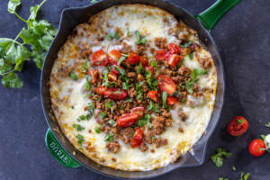 Queso Fundido in a skillet with herbs and tomato toppings.