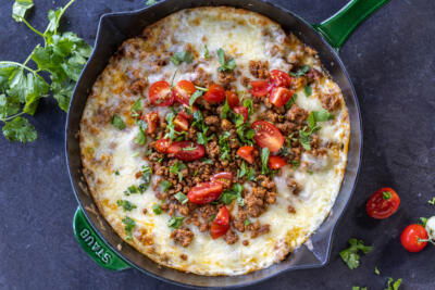 Queso Fundido in a skillet with herbs and tomato toppings.