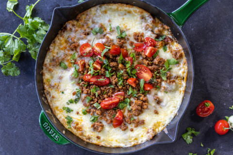 Queso Fundido in a skillet with herbs and tomato toppings.