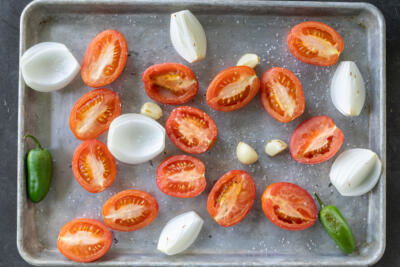 Tomatoes, onion, garlic and jalapeno on a baking sheet.