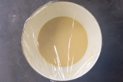 Crepe batter in a bowl with plastic wrap.