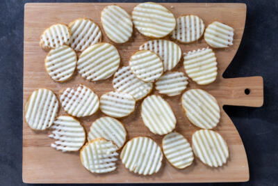 Waffle fries potatoes dried out on a cutting board.