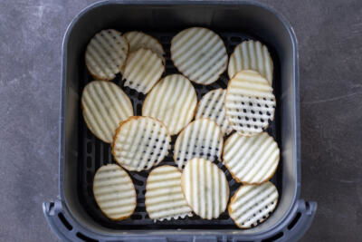 Waffle fries in an air fryer basket.