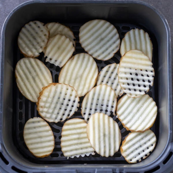 Waffle fries in an air fryer basket.