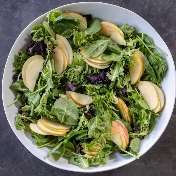 Sliced up apples in a bowl with leafy greens.