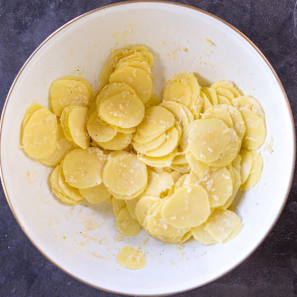 Parmesan added to sliced seasoned potatoes.