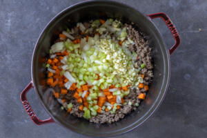 Veggies added to the meat in a pot.
