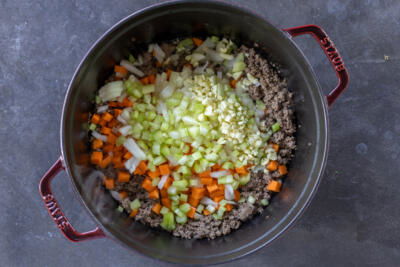 Veggies added to the meat in a pot.