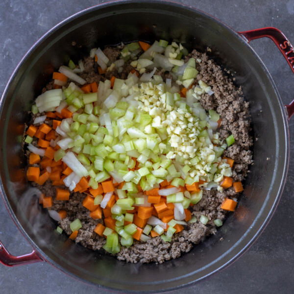 Veggies added to the meat in a pot.