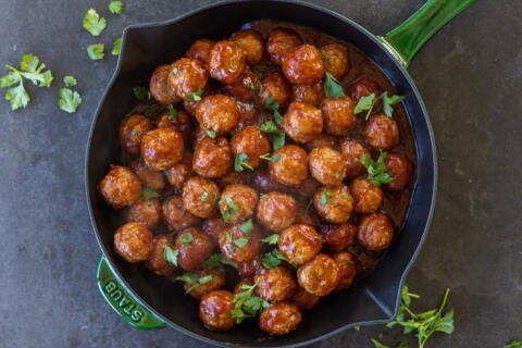 Cranberry Meatballs in a serving dish with herbs on top.