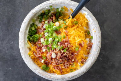 Cream, ranch seasoning, sour cream, cheese, bacon and green onions in a bowl.