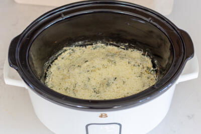 Spinach Artichoke Dip topped with cheese in a crock pot.