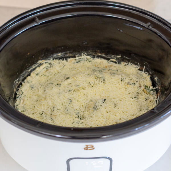 Spinach Artichoke Dip topped with cheese in a crock pot.