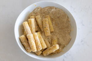 Cheese sticks covered in crumbs in a bowl.