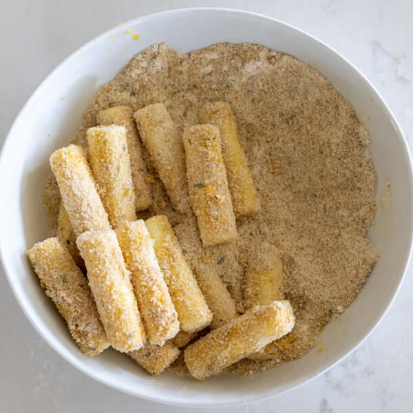 Cheese sticks covered in crumbs in a bowl.