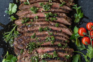 Chimichurri Steak sliced on a serving tray and herbs.