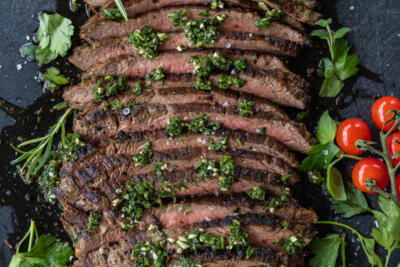 Chimichurri Steak sliced on a serving tray and herbs.