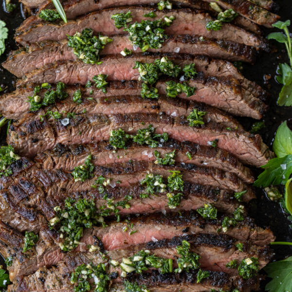 Chimichurri Steak sliced on a serving tray and herbs.